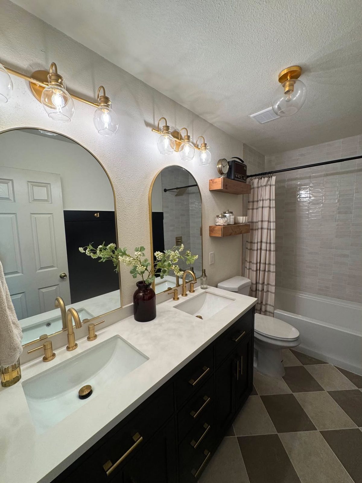 Double vanity with black cabinets, arched gold mirrors and a checkered floor