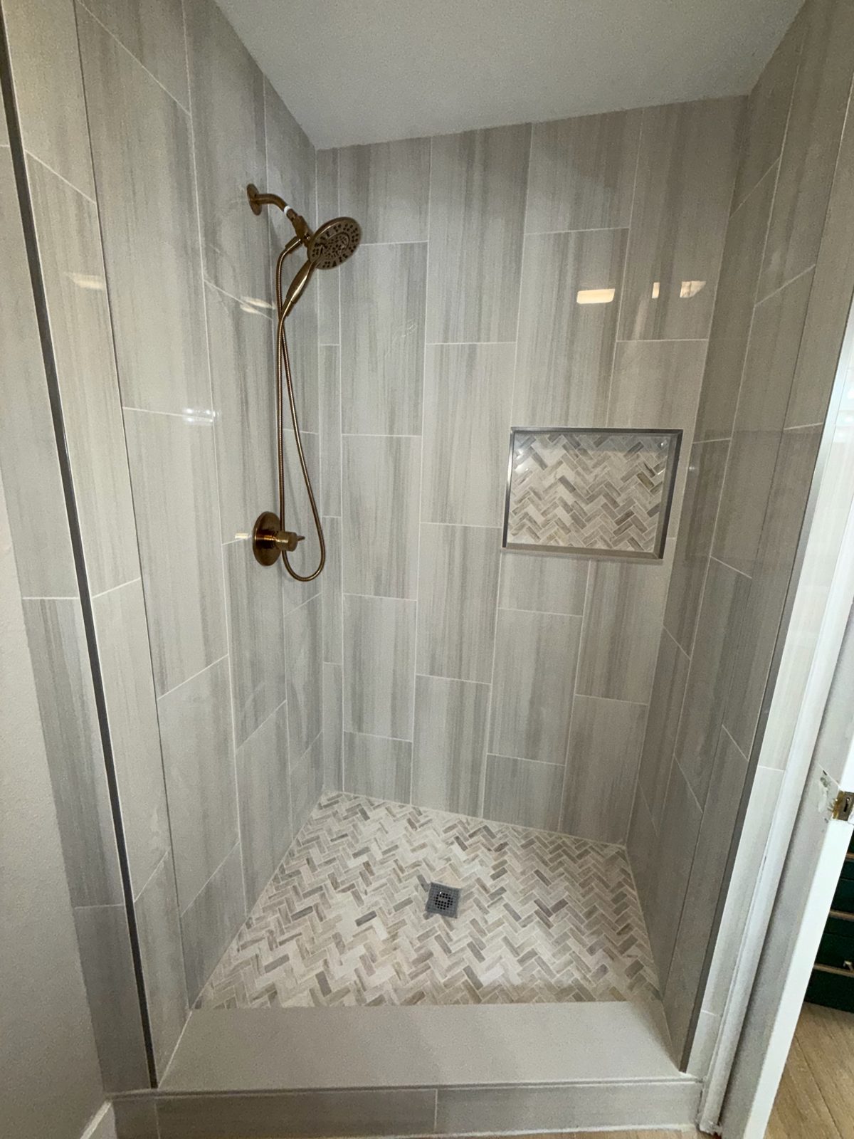 Walk-in shower with grey plank tile, herringbone niche and floor, and bronze fixtures