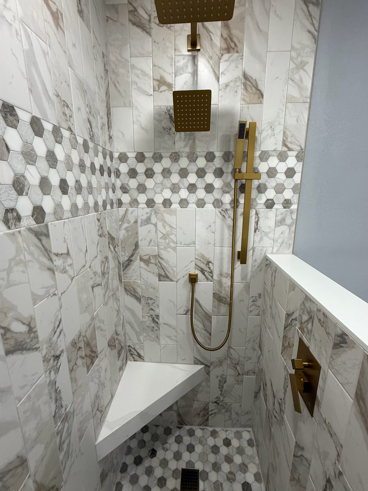 Marble-look shower with a corner bench and gold fixtures