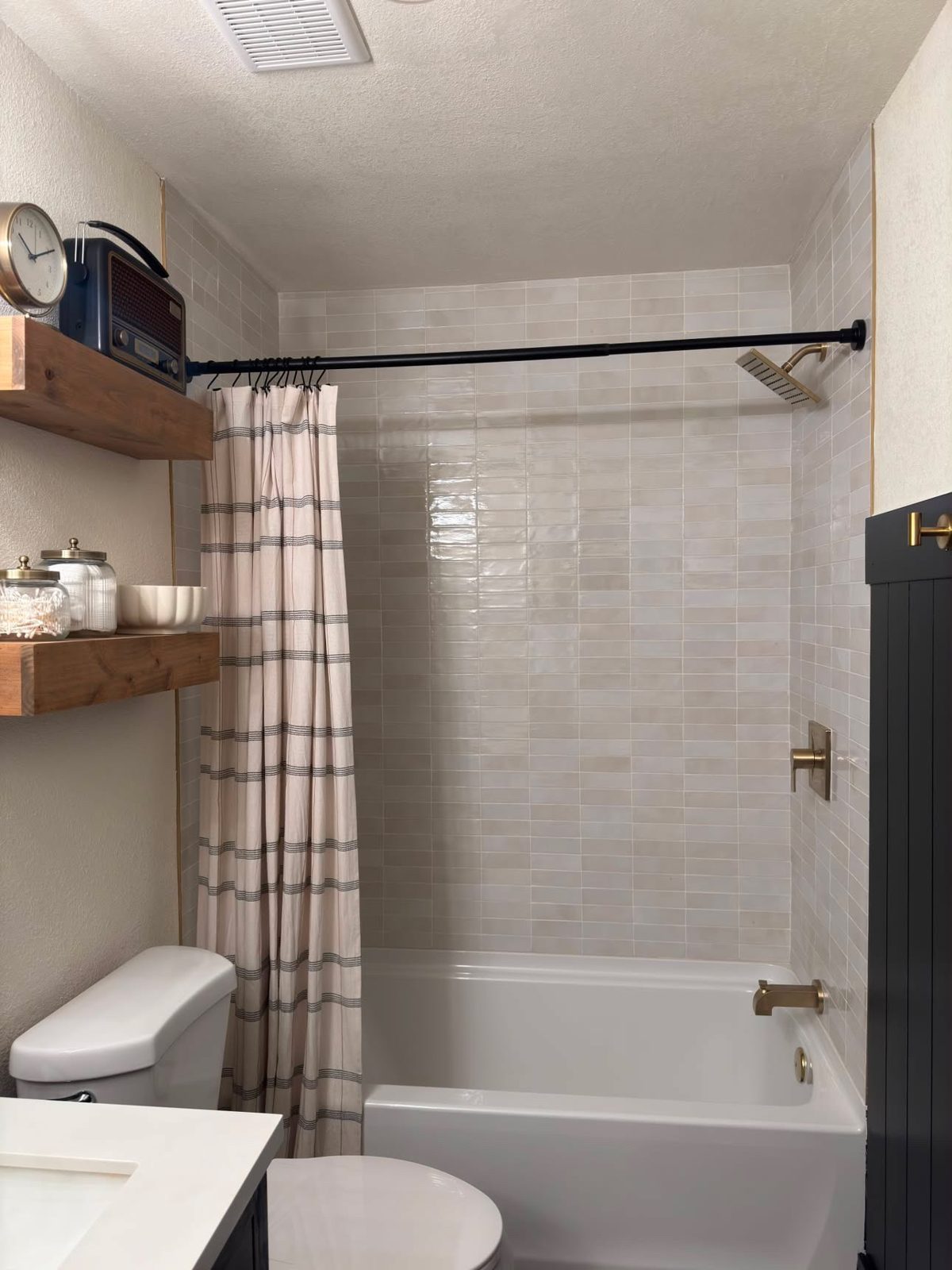 Bathtub surround in glossy zellige-style tile with floating wood shelves