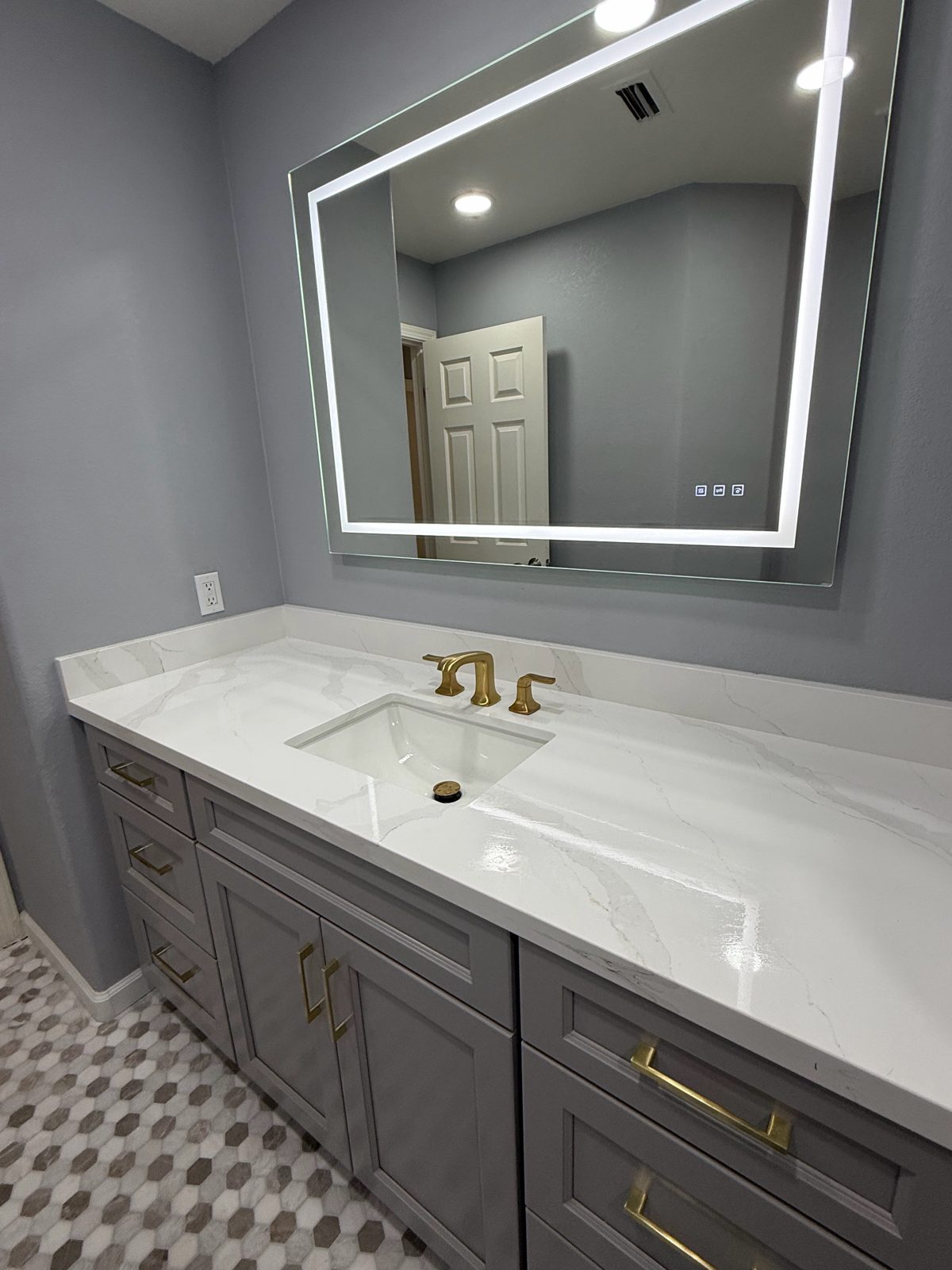 Grey shaker vanity with a quartz top, LED mirror and gold hardware